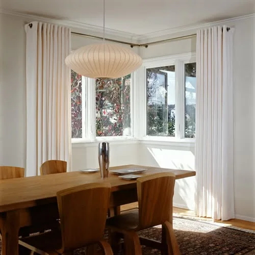 White custom drapery installed around a dining room bay window